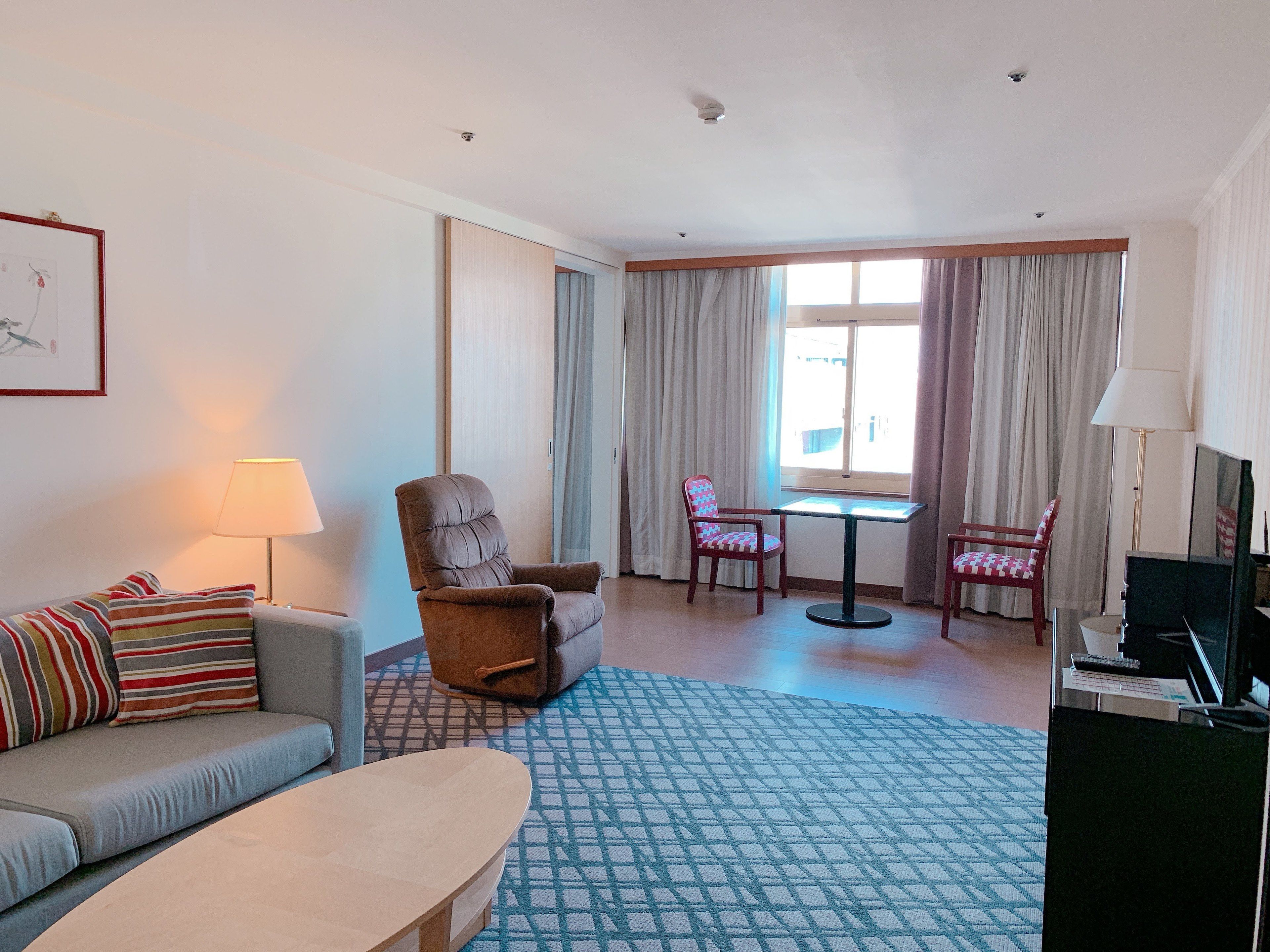 A hotel room with a sofa, armchair, dining table, and chairs.