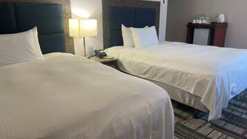 A hotel room with two beds, a nightstand with a lamp, and a small table with a coffee maker.