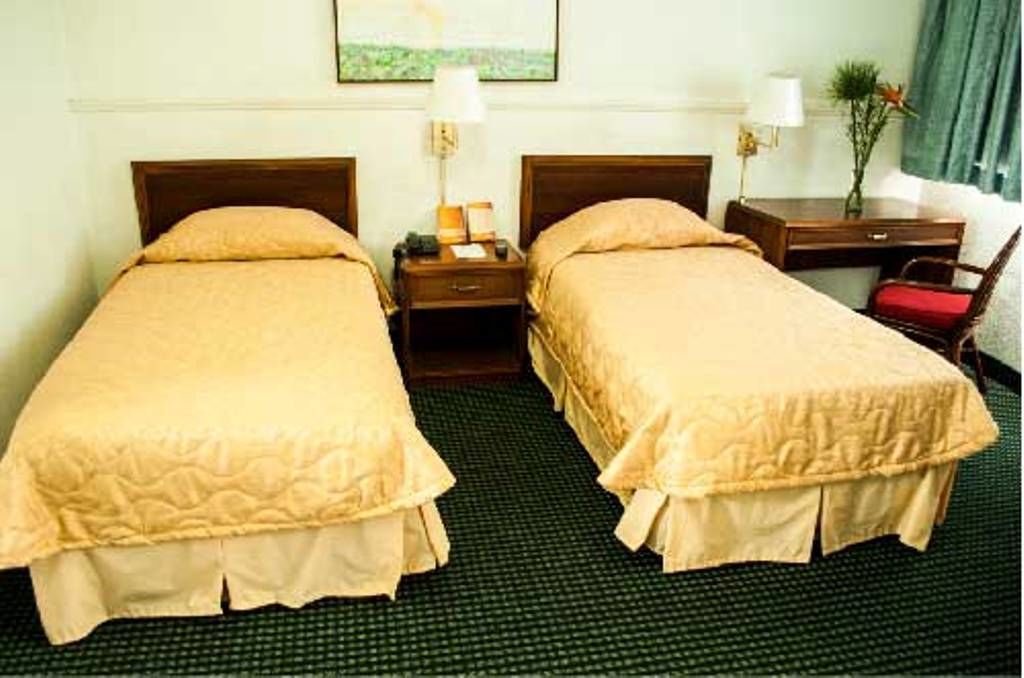 A hotel room with two single beds, a desk, a chair, and a nightstand with lamps.