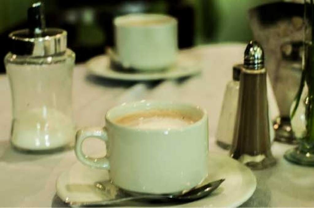 A table with a cup of coffee, a sugar container, a salt shaker, and a creamer dispenser.
