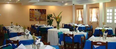 A dining area with round tables covered in blue tablecloths, white table settings, and wooden chairs.