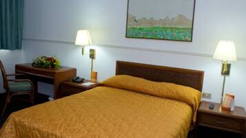 Habitación de hotel con cama, dos mesitas de noche, un escritorio con silla, una lámpara y un cuadro en la pared.