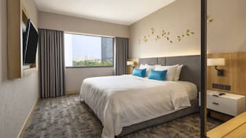 Una habitación de hotel con una cama grande, un televisor montado en la pared, una ventana con cortinas y vistas a la ciudad.