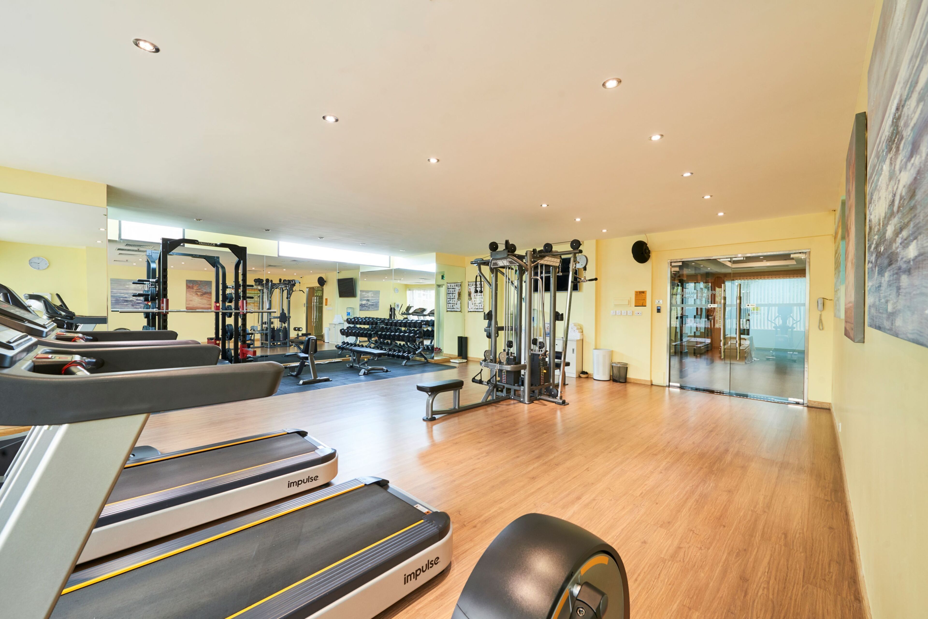 Un gimnasio con cintas de correr, máquinas de pesas y un espejo grande.