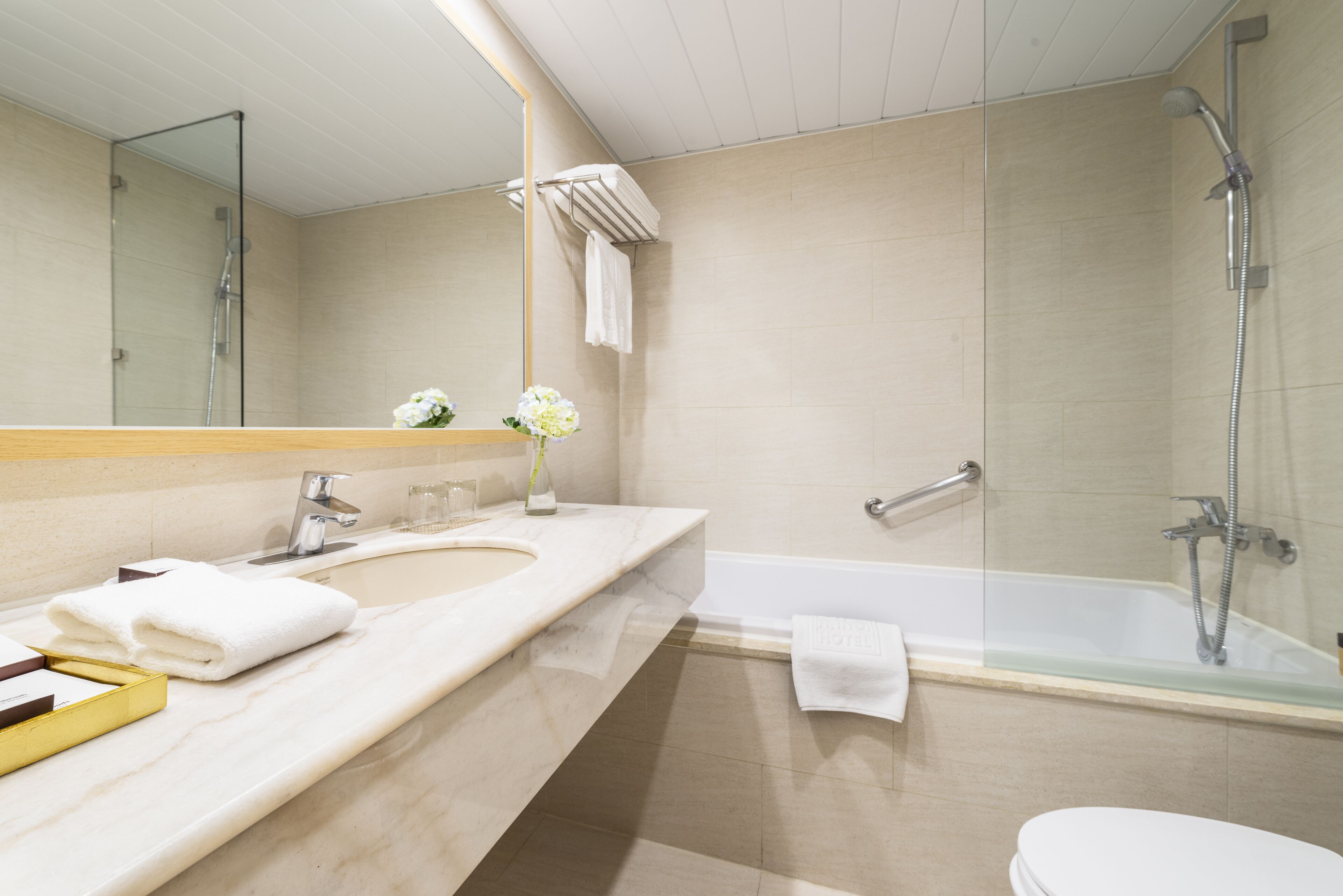 A modern bathroom with a large mirror, a bathtub, a shower, and a toilet.