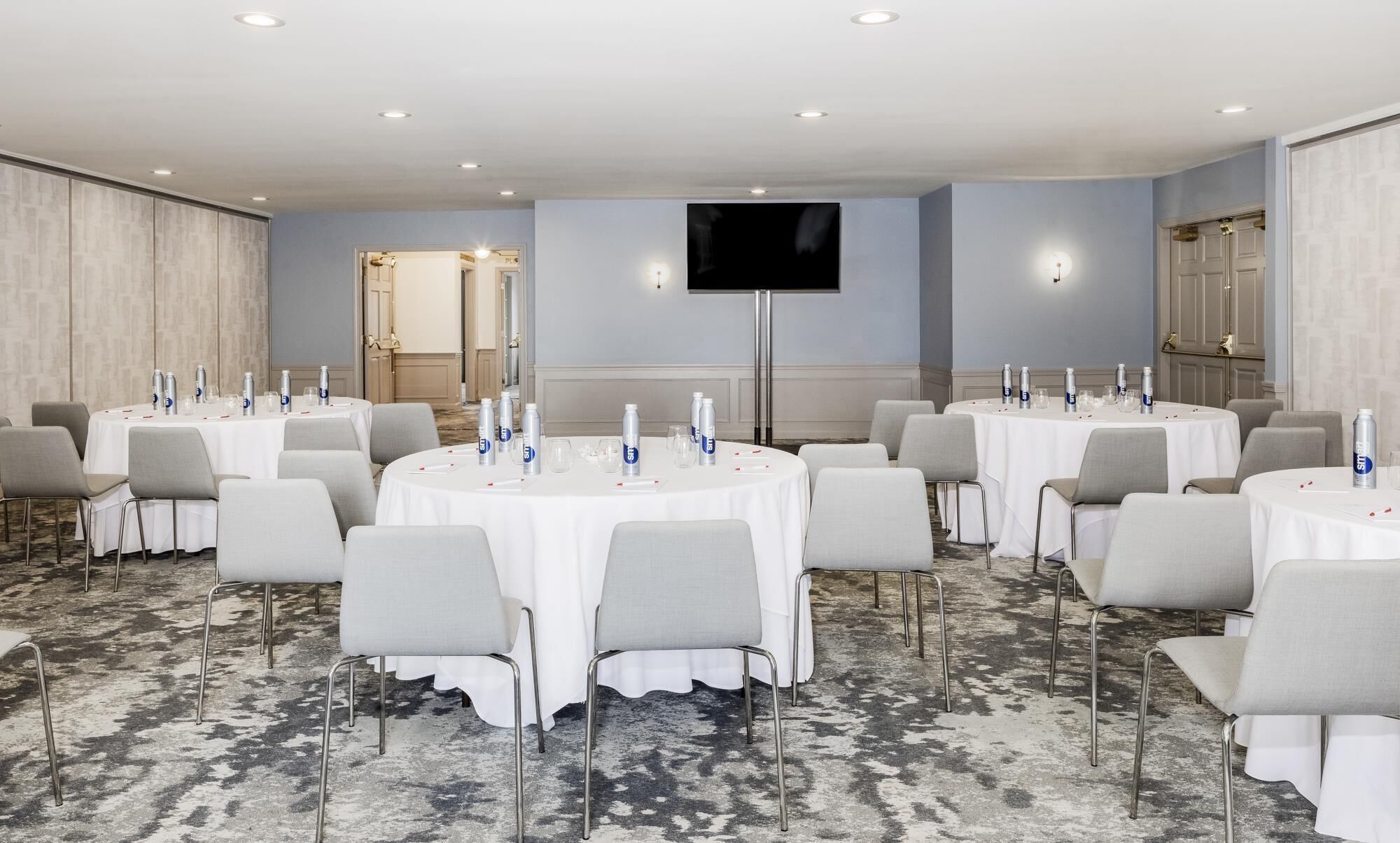 Un salón de conferencias con mesas redondas, sillas grises y un televisor de pantalla plana montado en la pared.