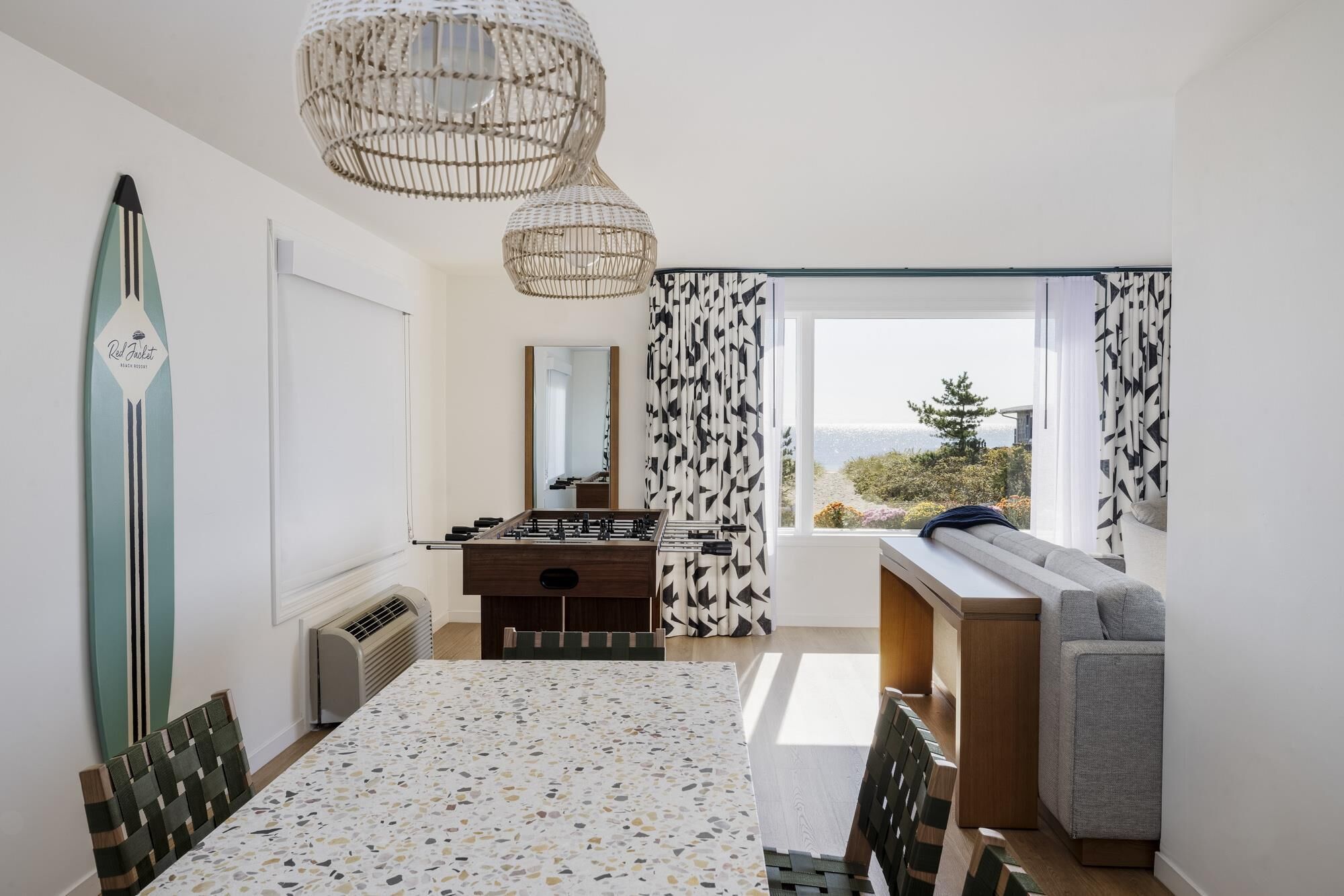 Une chambre comprenant un lit, un futon, un miroir, une fenêtre avec des rideaux, une table de baby-foot et un étagère fixée au mur.