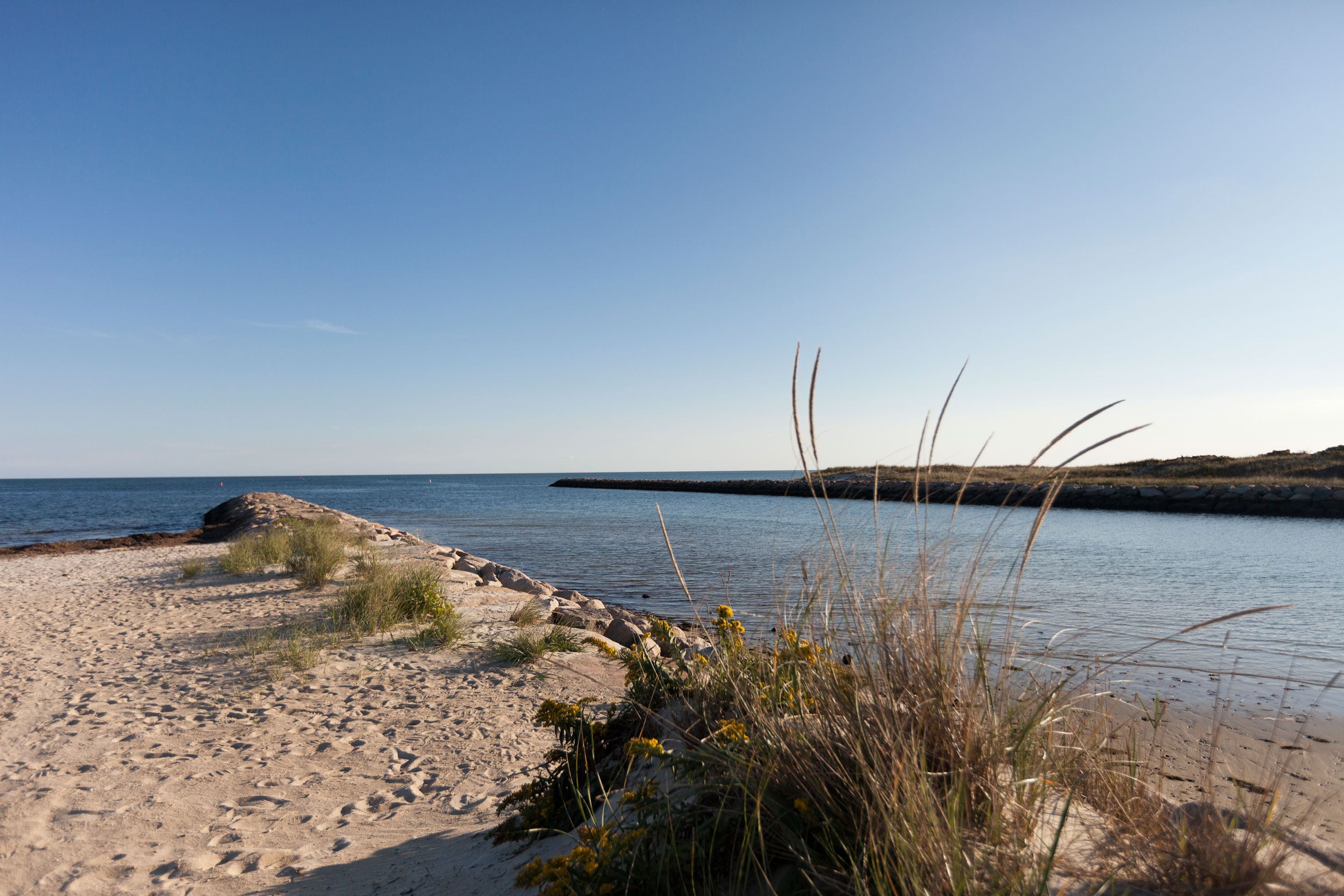 A sandy beach with clear blue water and a rocky outcrop in the distance.