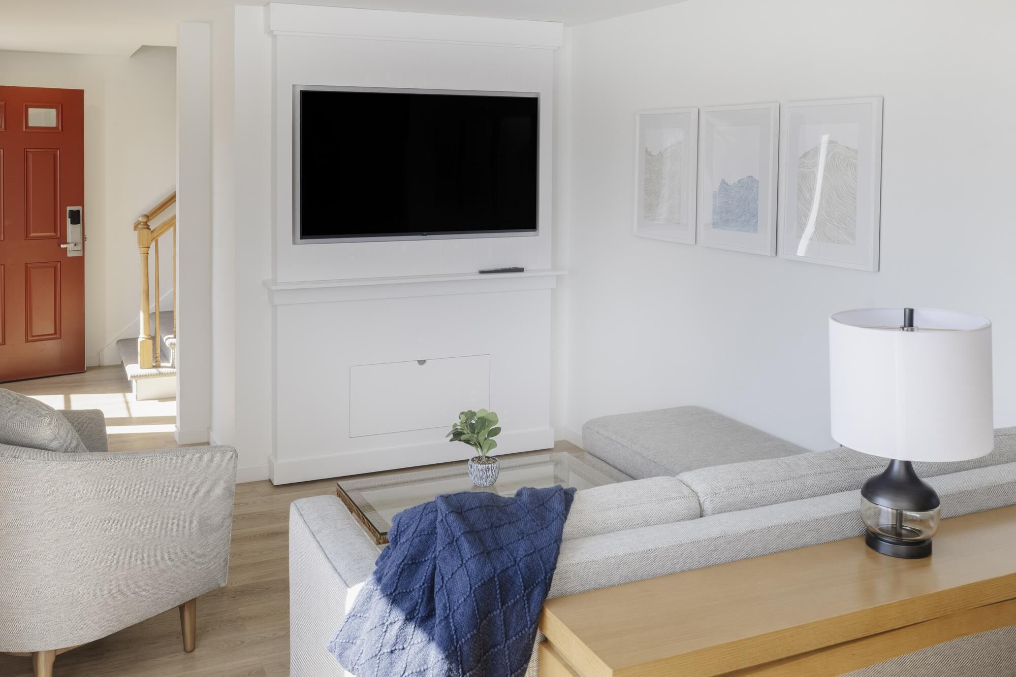 A modern living room with a flat-screen TV mounted on a white wall, a sofa, a coffee table, and a lamp.