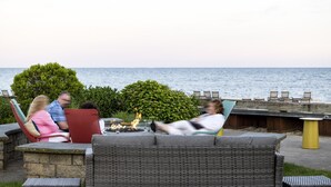 Un espace extérieur aménagé avec des meubles en osier, un foyer et une vue sur la mer.