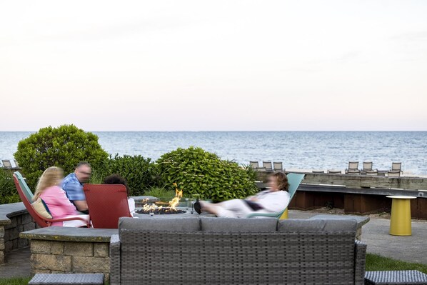 A patio area with wicker furniture, a fire pit, and a view of the sea.