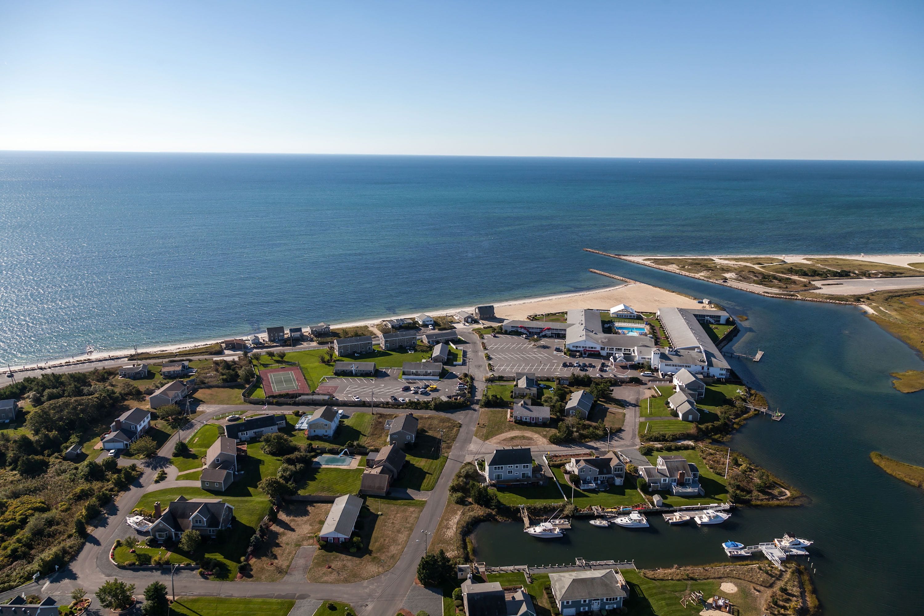 Vue aérienne d’une zone résidentielle côtière, avec des maisons, une plage et un port de plaisance.