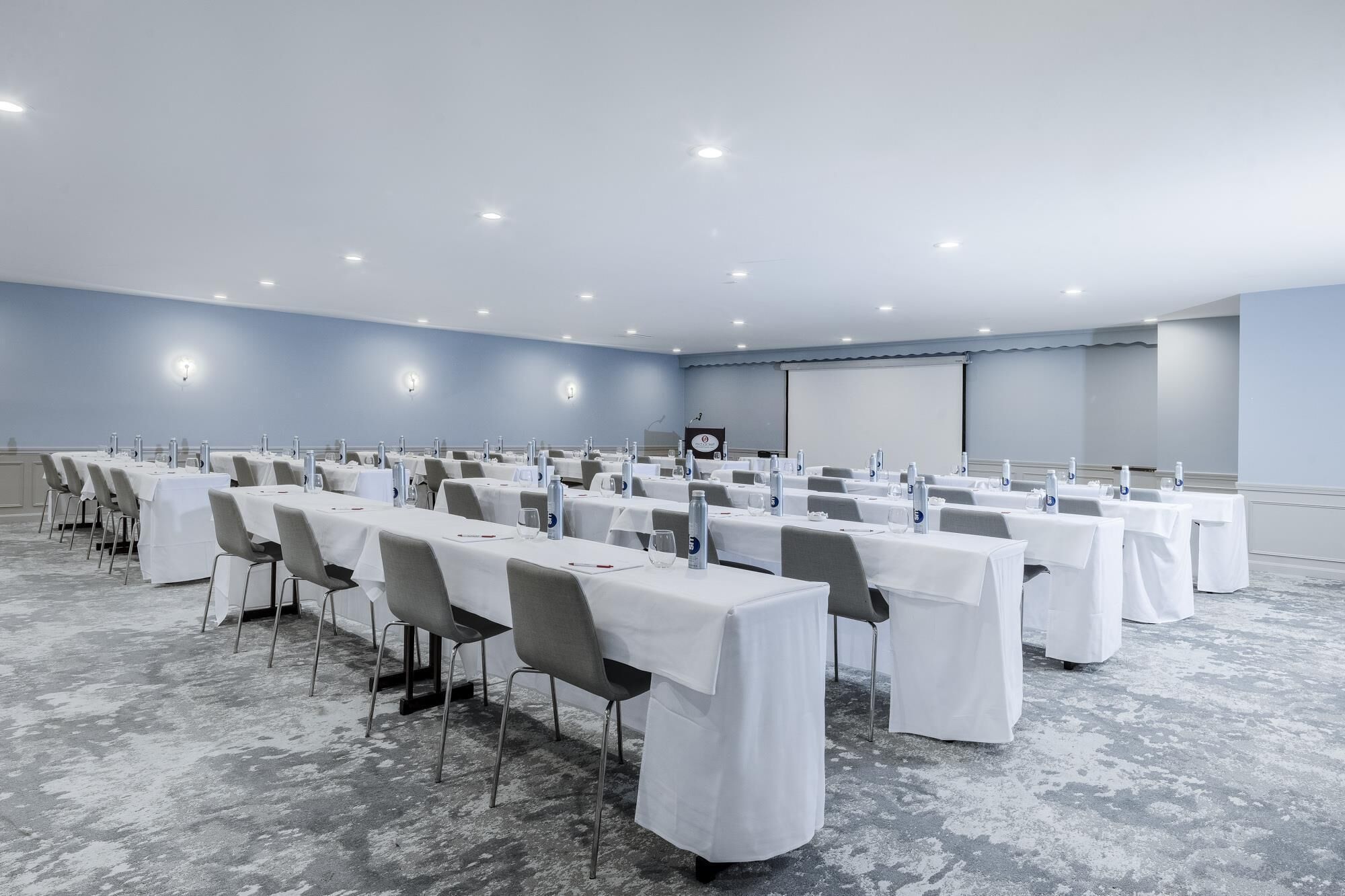 A conference room with rows of tables, chairs, and a presentation screen.