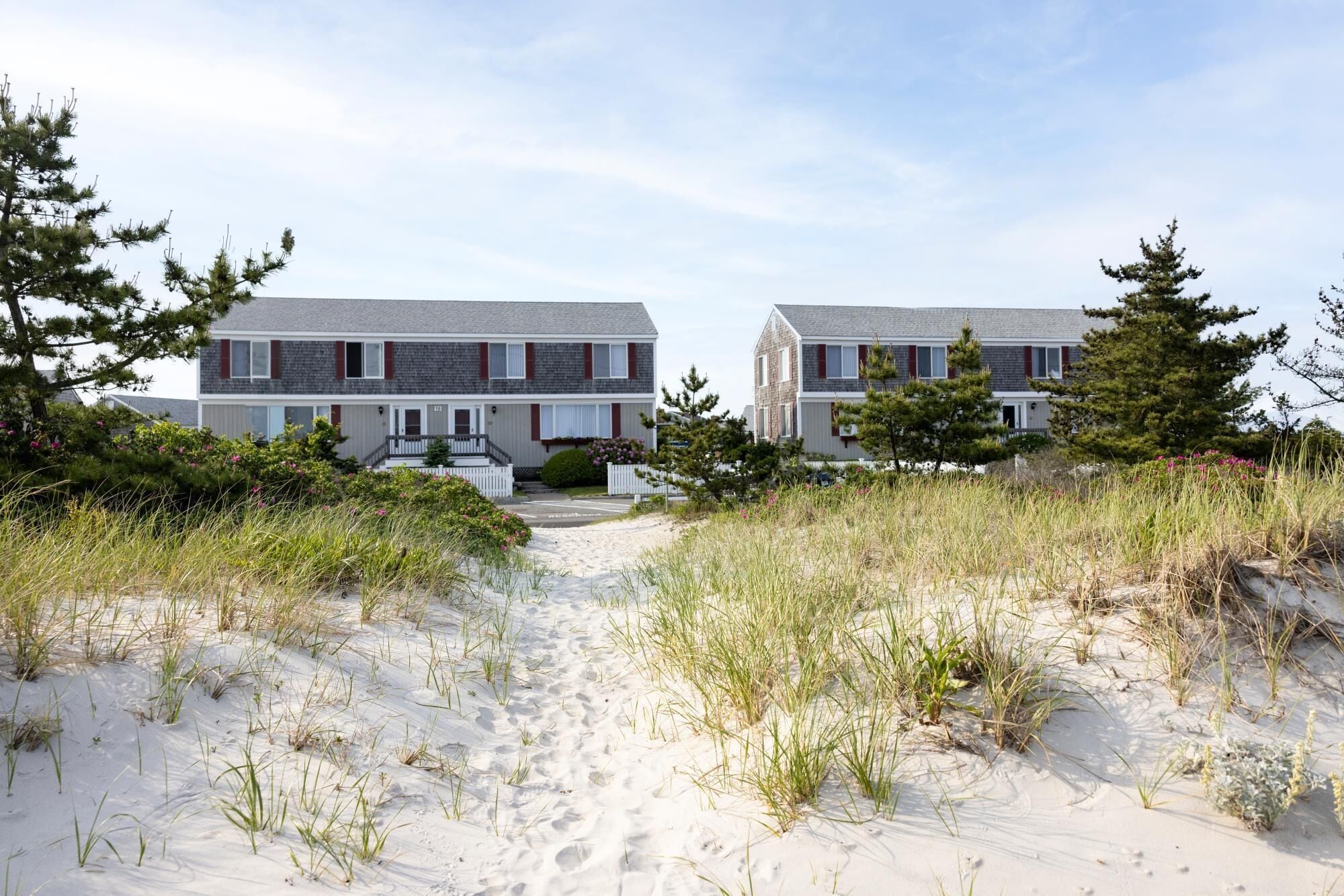 Una propiedad frente a la playa con casas de dos pisos, senderos de arena y vegetación circundante.