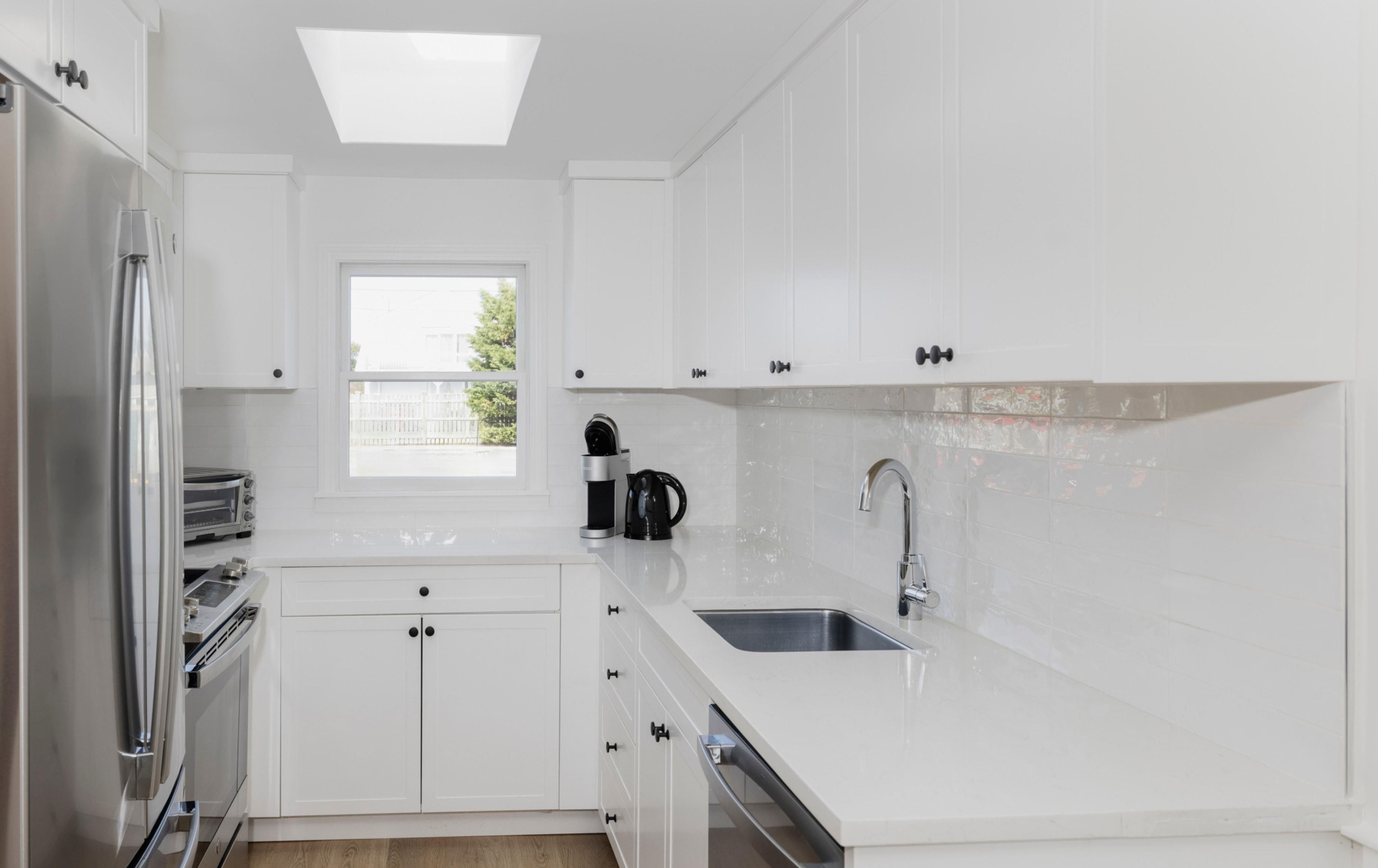 Una cocina moderna con armarios blancos, horno empotrado, cafetera y ventana.