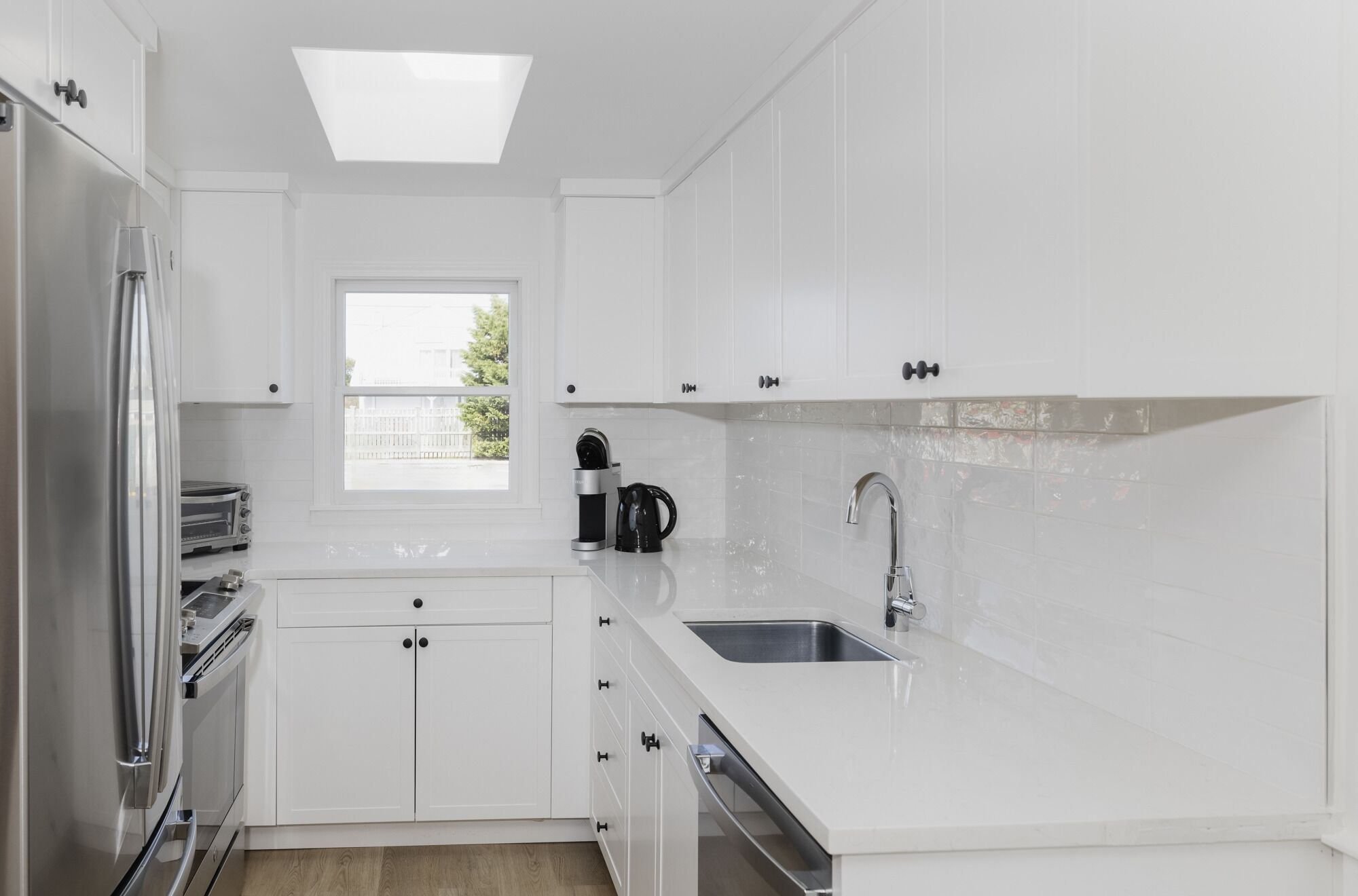 Una cocina moderna con armarios blancos, horno integrado, lavamanos y ventana que proporciona luz natural.