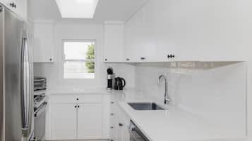 Una cocina moderna con armarios blancos, horno integrado, lavamanos y ventana que proporciona luz natural.