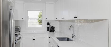Una cocina moderna con armarios blancos, horno integrado, lavamanos y ventana que proporciona luz natural.