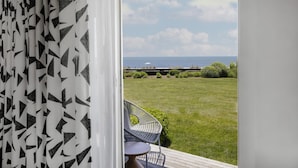 A balcony with a view of the sea, a grassy lawn, and a chair.