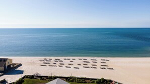 Une plage bordée de rangées de chaises longues et un bâtiment doté d’un toit en pente.