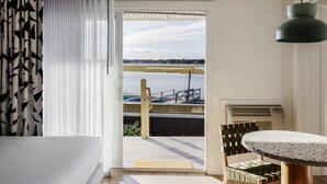 Une pièce avec vue sur un quai et l’eau, une table recouverte d’une nappe à motifs et une suspension décorative au plafond.