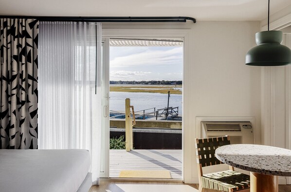 A room with a view of a dock and water, a table with a patterned tablecloth, and a hanging pendant light. - Red Jacket Beach Resort (South Yarmouth)