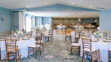 A spacious banquet hall with round tables and wooden chairs, featuring a blue ceiling and a carpeted floor.