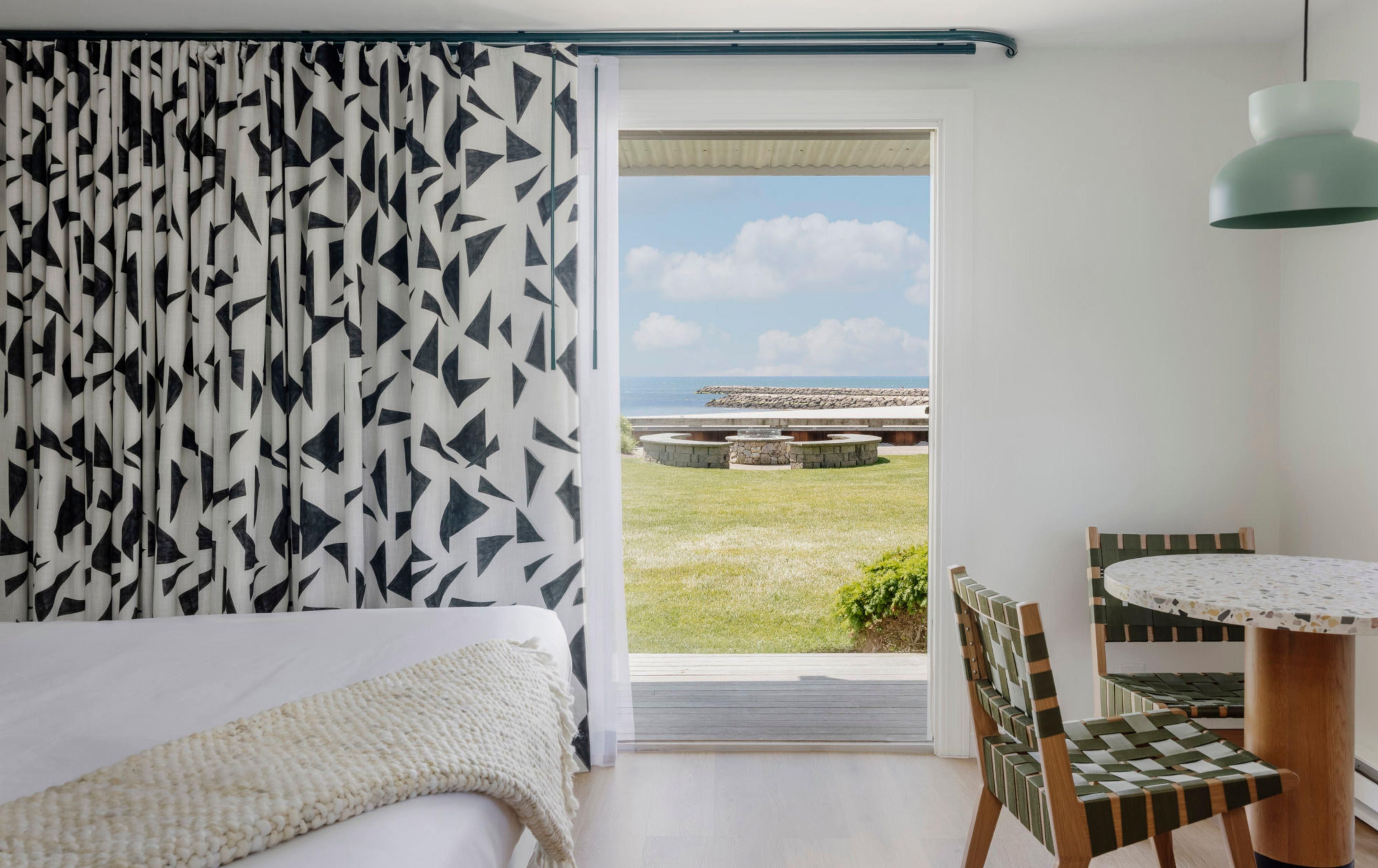 Un dormitorio con cama, vistas al exterior, zona de comedor con mesa y sillas, y lámpara colgante.