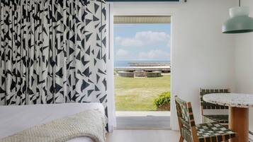 Un dormitorio con cama, vistas al exterior, zona de comedor con mesa y sillas, y lámpara colgante.
