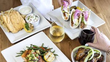 A variety of dishes including fish, tacos, and a salad, along with two glasses of wine on a wooden table.