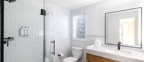 Une salle de bain moderne avec une douche à parois de verre, des toilettes, un lavabo avec un miroir et une fenêtre équipée de stores.