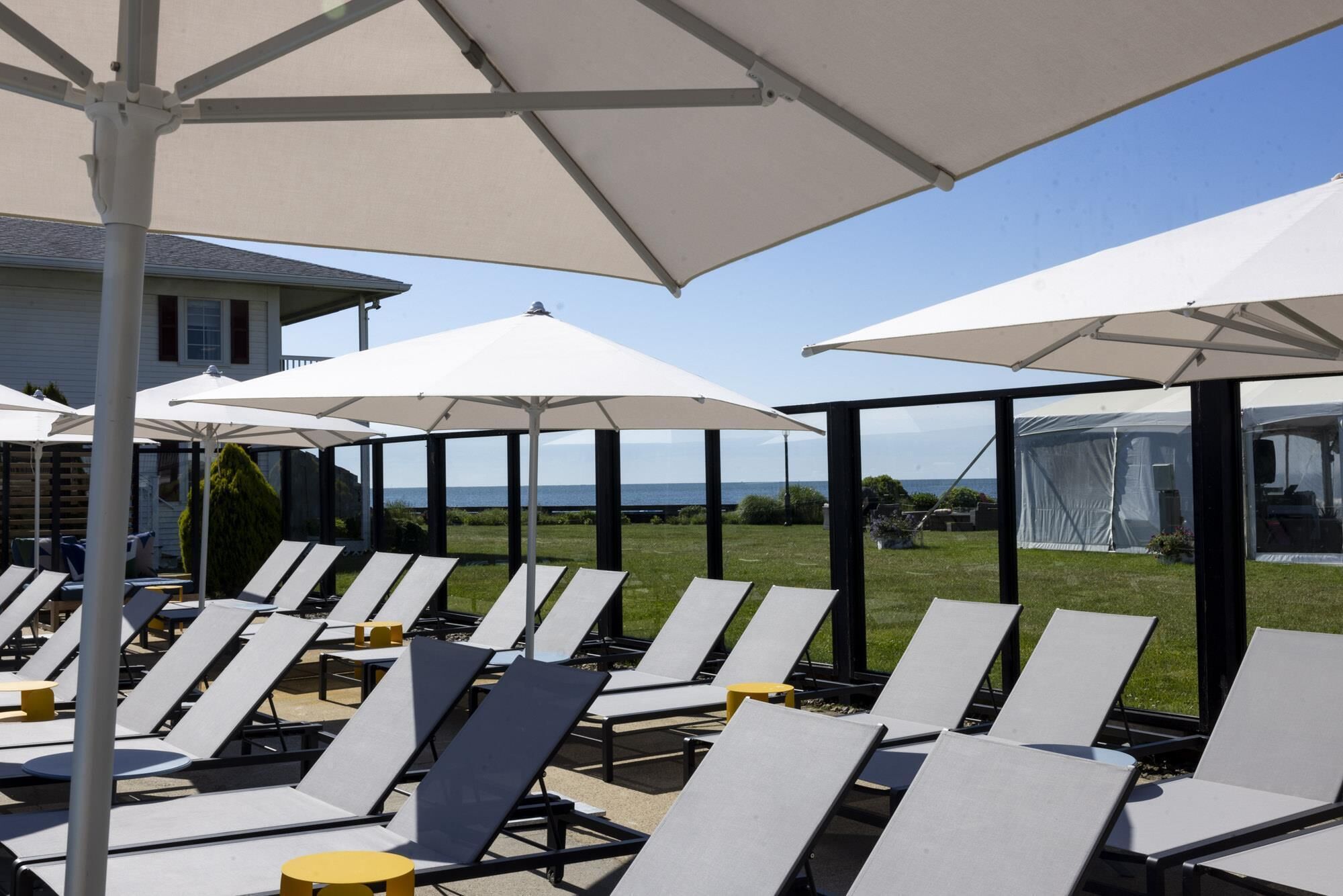Eine Terrasse mit Liegestühlen und Sonnenschirmen, mit Blick auf eine Rasenfläche und ein Gewässer.