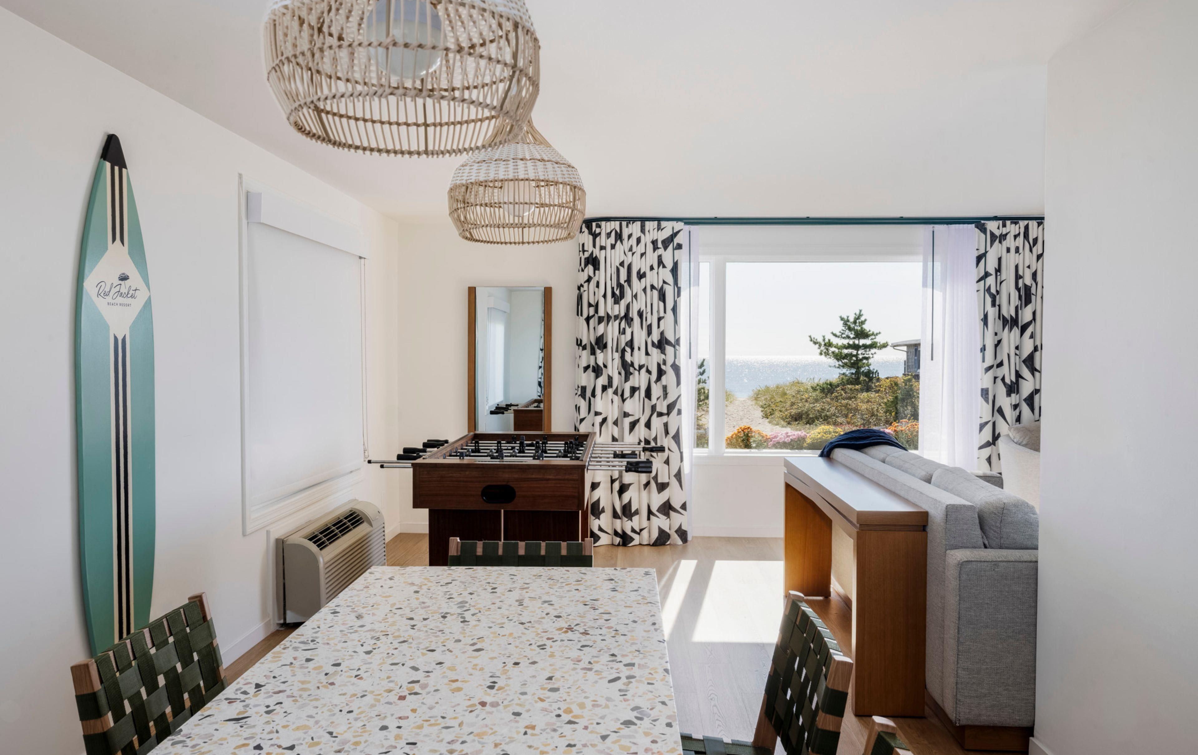 Une pièce avec une table de baby-foot, un canapé, une fenêtre donnant sur un beau paysage et un ventilateur de plafond.
