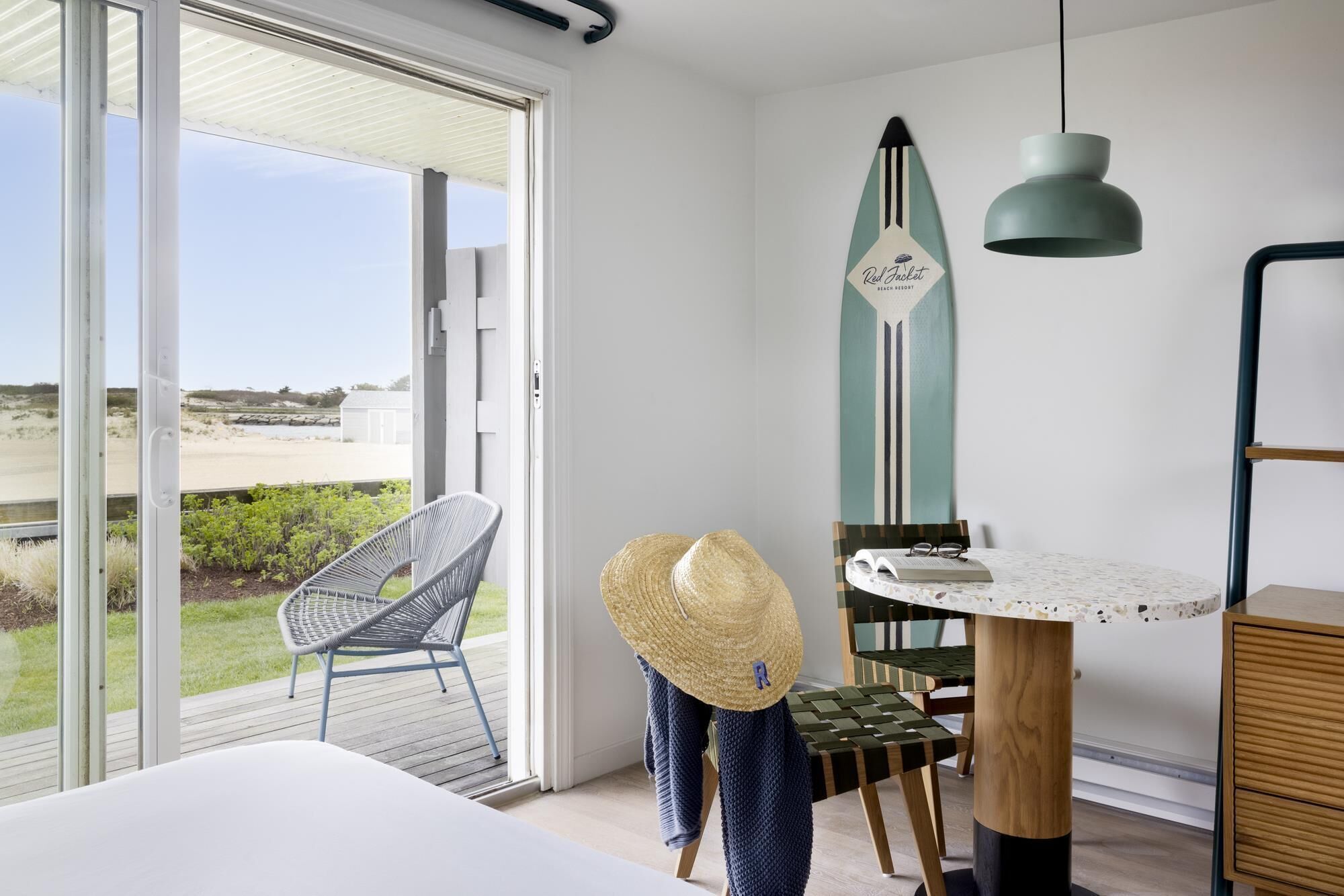 Una habitación con cama, una mesa de comedor con sillas, un sombrero y una lámpara colgante.