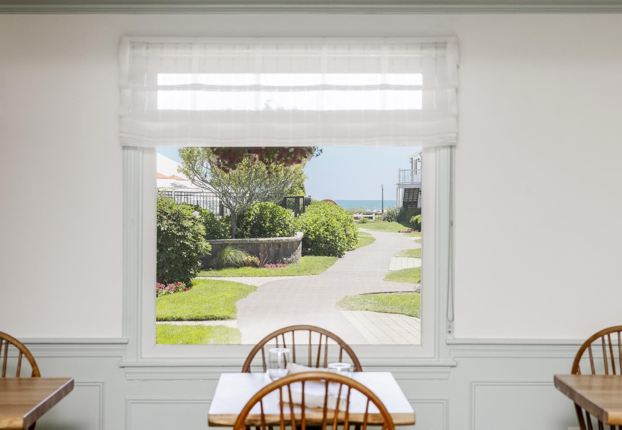 Une chambre avec une fenêtre donnant sur un jardin et un sentier menant à la mer.