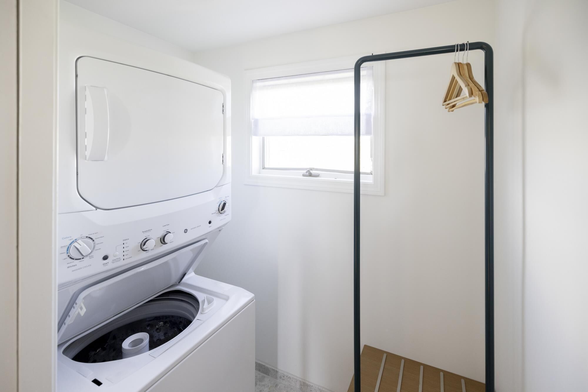 A laundry room with a washing machine and dryer, a window, and a drying rack with clothes.