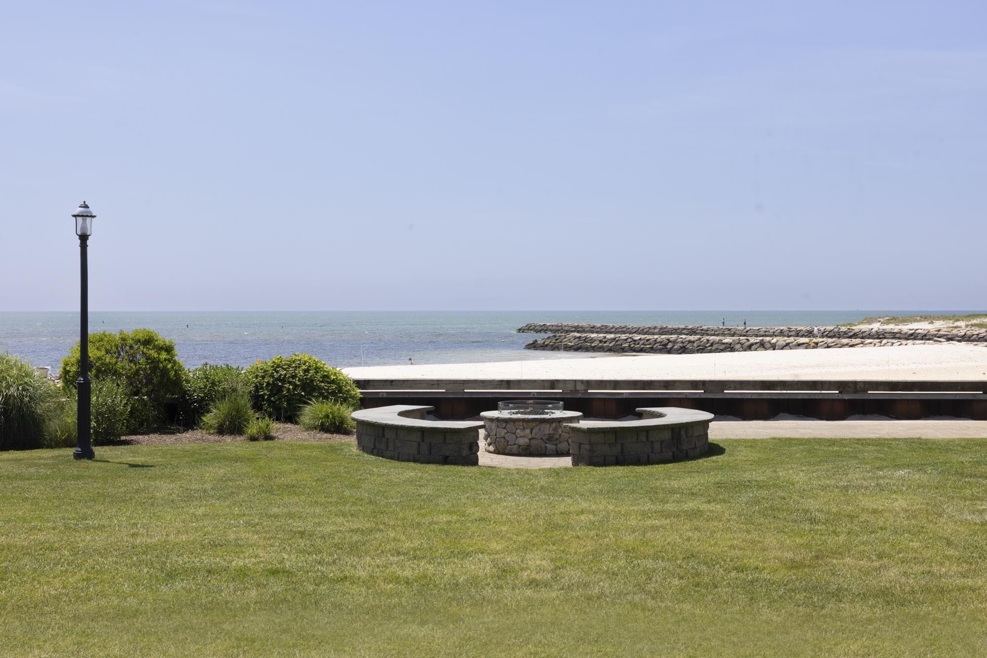 A coastal park with a stone bench area, a lamp post, and a view of the sea.