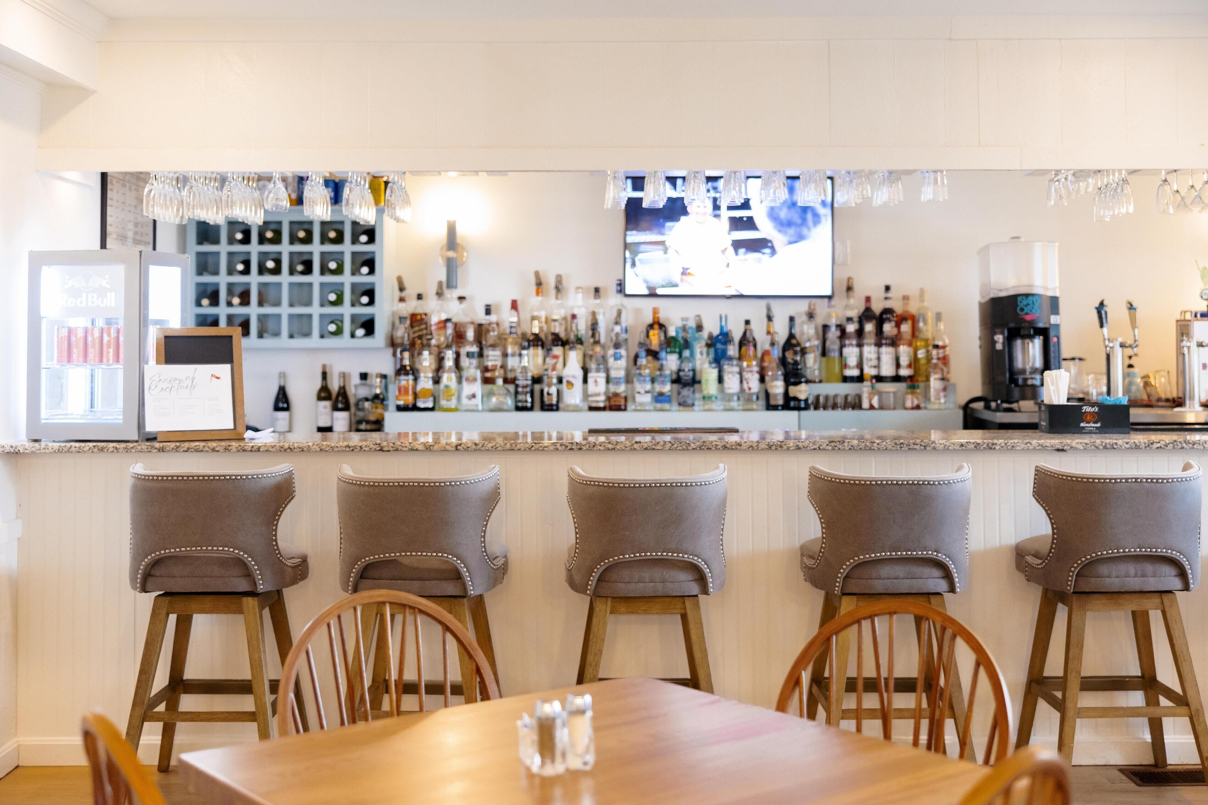 A bar area with a long counter, multiple stools, and a television screen.