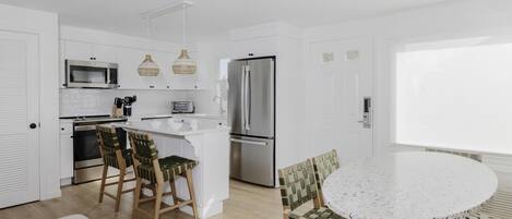 Uma cozinha moderna com armários brancos, eletrodomésticos de aço inoxidável e uma ilha central com banquetas.
