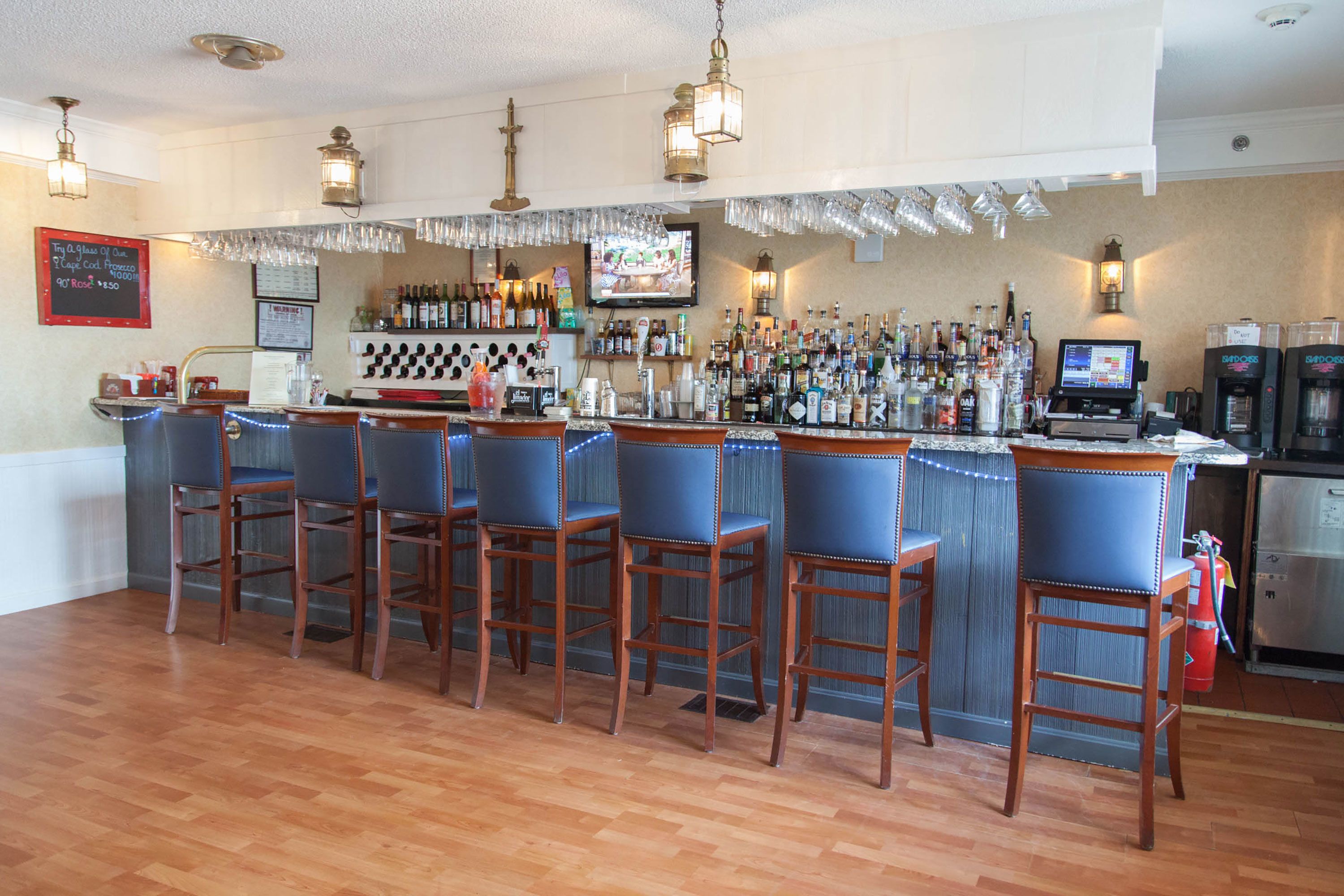 A bar area with wooden bar stools, a television screen, and a variety of bottles and glasses on the shelves.