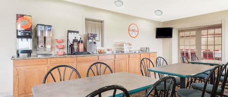 A hotel dining area with a counter, coffee machines, and seating.
