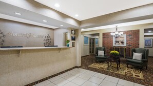 A reception area with a reception desk, two green armchairs, a patterned rug, and a chandelier. - Howard Johnson by Wyndham Springfield (Springfield)