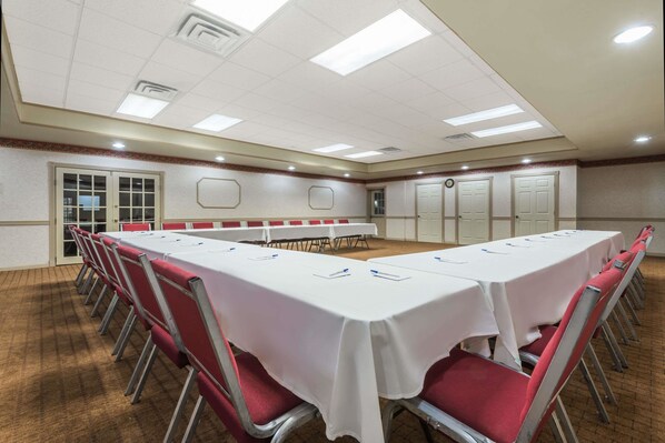 A conference room with a long table, red chairs, and white walls.