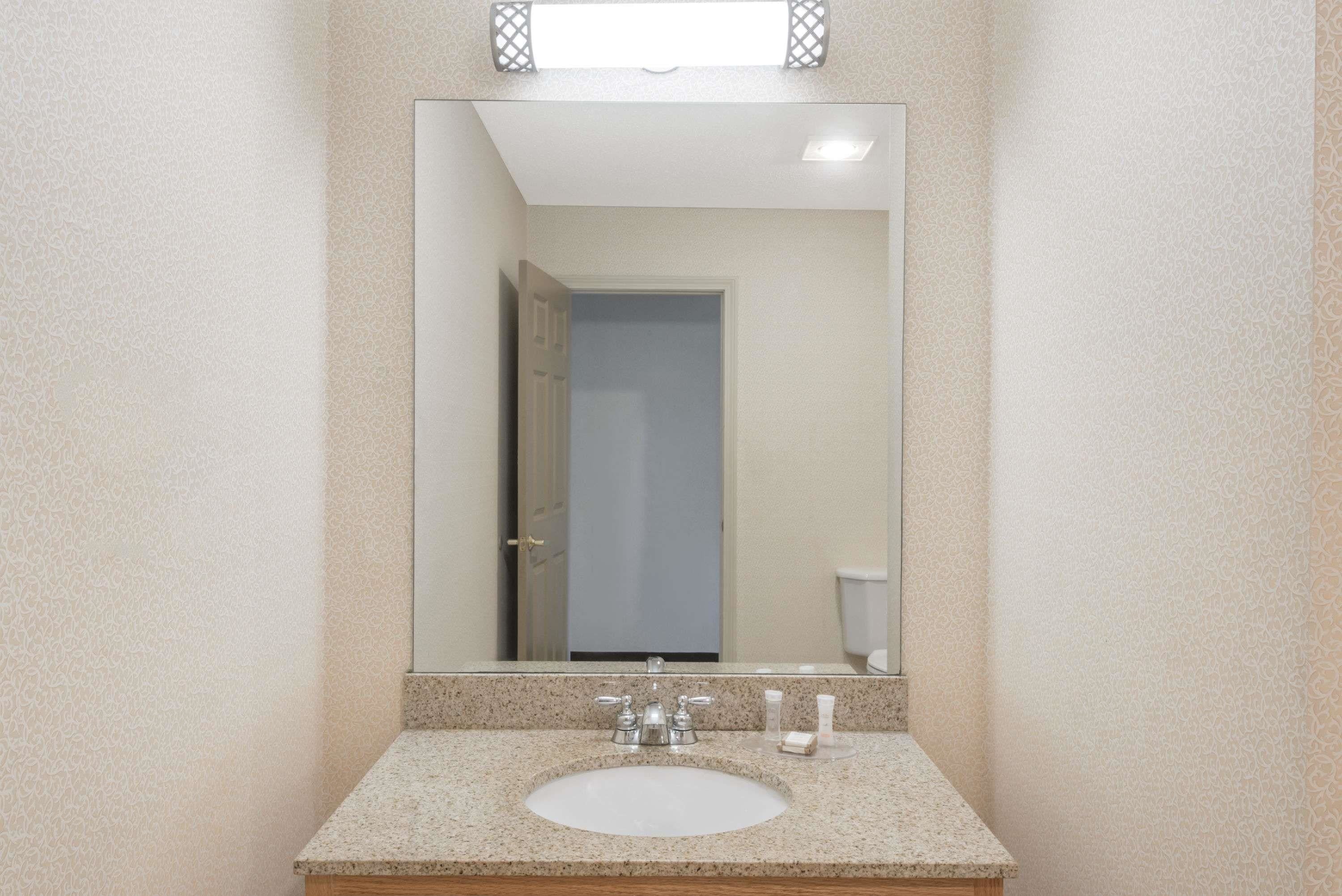 Une salle de bain avec un comptoir en granit, un lavabo blanc et un miroir au-dessus.