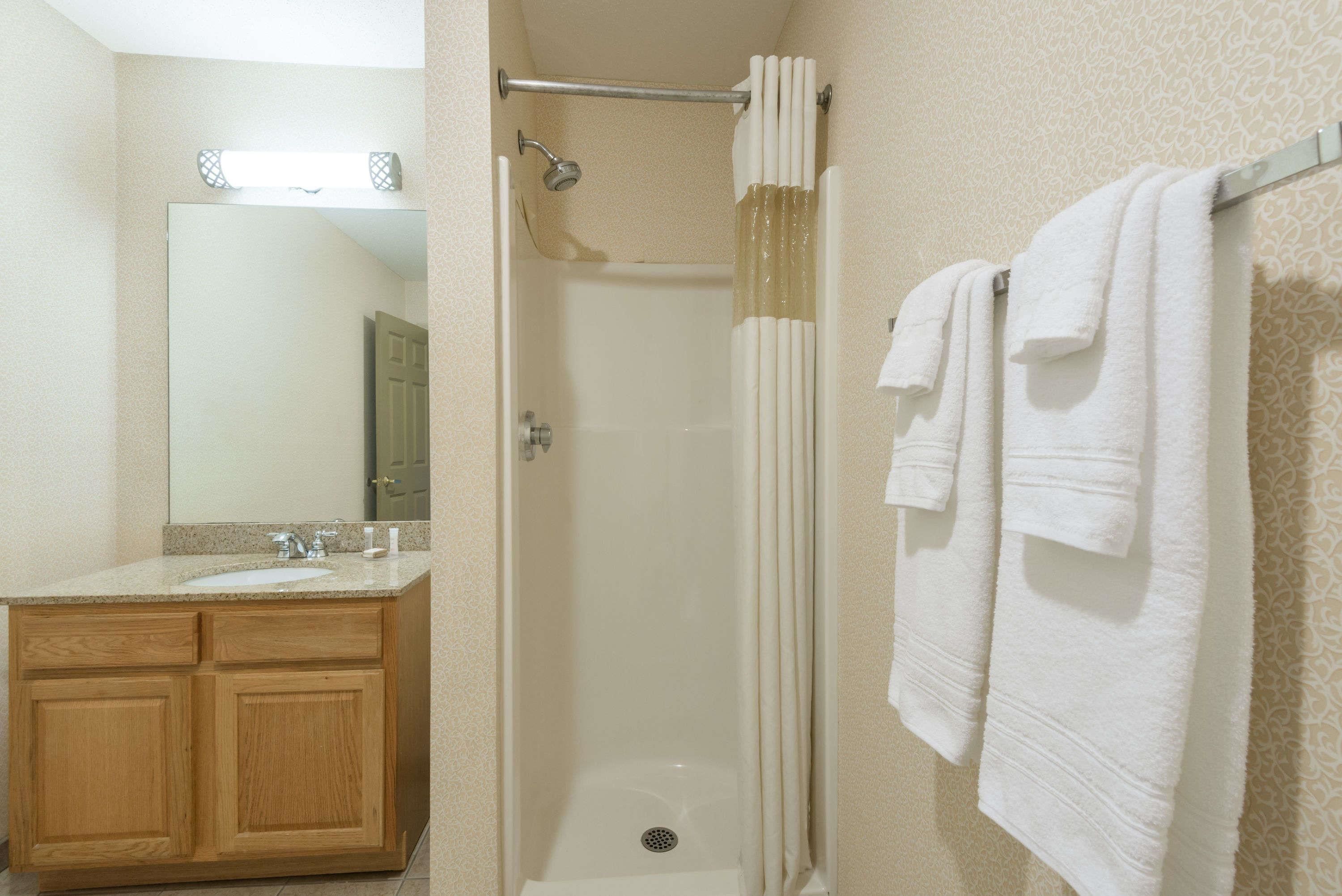 A bathroom with a shower, a sink, and a mirror. There are towels hanging on a rack.