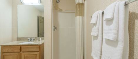 A bathroom with a shower, a sink, and a mirror. There are towels hanging on a rack.
