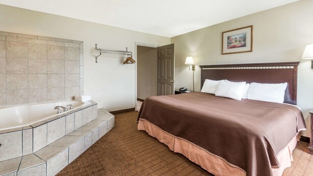 A hotel room with a large bathtub, a bed with a brown headboard, and a painting on the wall. - Howard Johnson by Wyndham Springfield (Springfield)