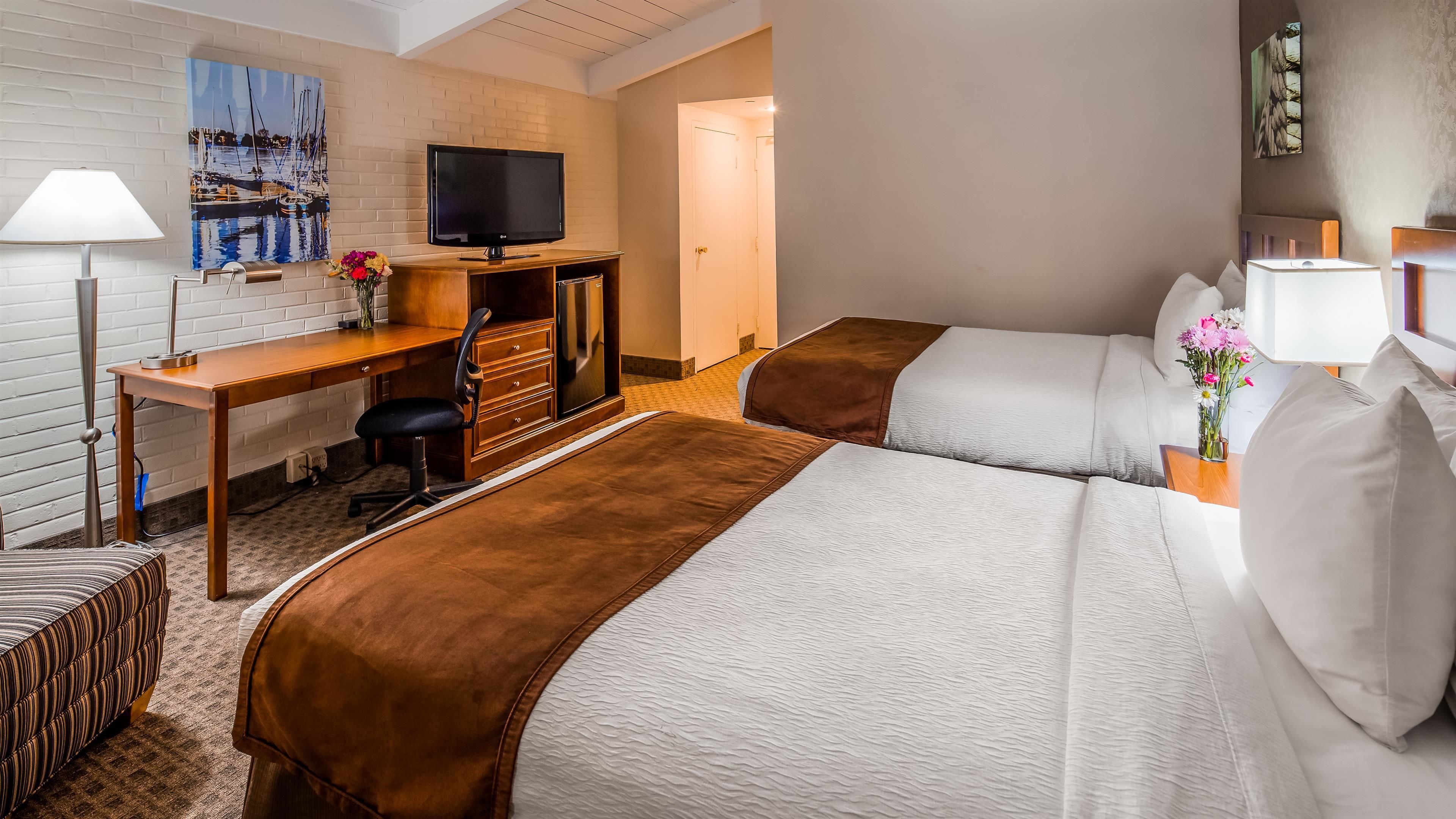 A hotel room with two beds, a desk with a TV, a lamp, and a painting on the wall.