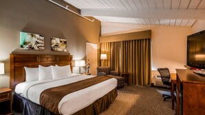 A hotel room with a large bed, a desk with a chair, a television, and a window with curtains.