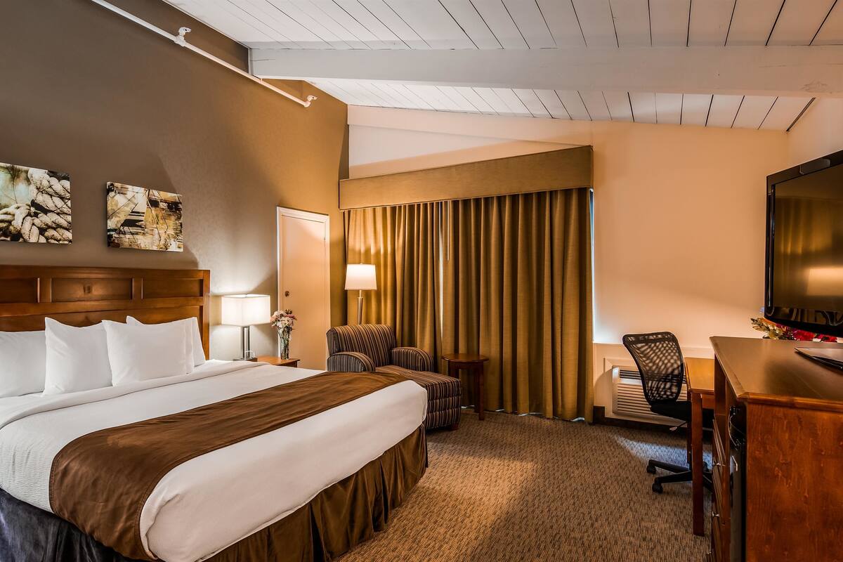 A hotel room with a large bed, a desk with a chair, a television, and a window with curtains.